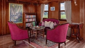 A room with wooden paneling, a bookshelf, a red armchair, a round table, and a window with curtains. - Dahabeya Farouz El Nil 3 (Al Bairat)