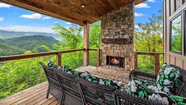 A covered outdoor area with a stone fireplace, wicker furniture, and a view of the mountains.