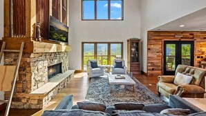 A spacious living room with a stone fireplace, large windows, and a view of the outdoors.