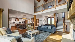 A spacious living area with a high ceiling, a dining area, and a staircase leading to an upper level.