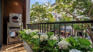 Un balcon avec un lave-linge, des plantes en pot et une vue sur des immeubles et des arbres.