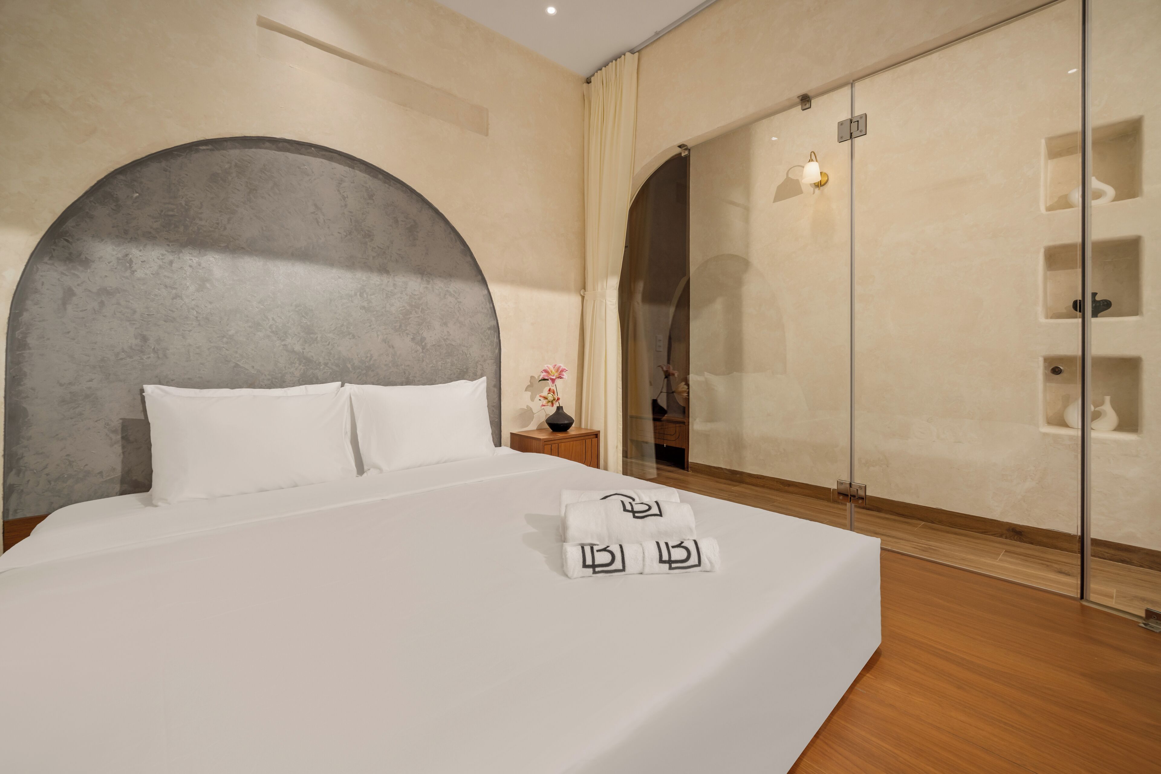 A modern hotel room with a large bed, a glass-enclosed walk-in closet, and a minimalist design.