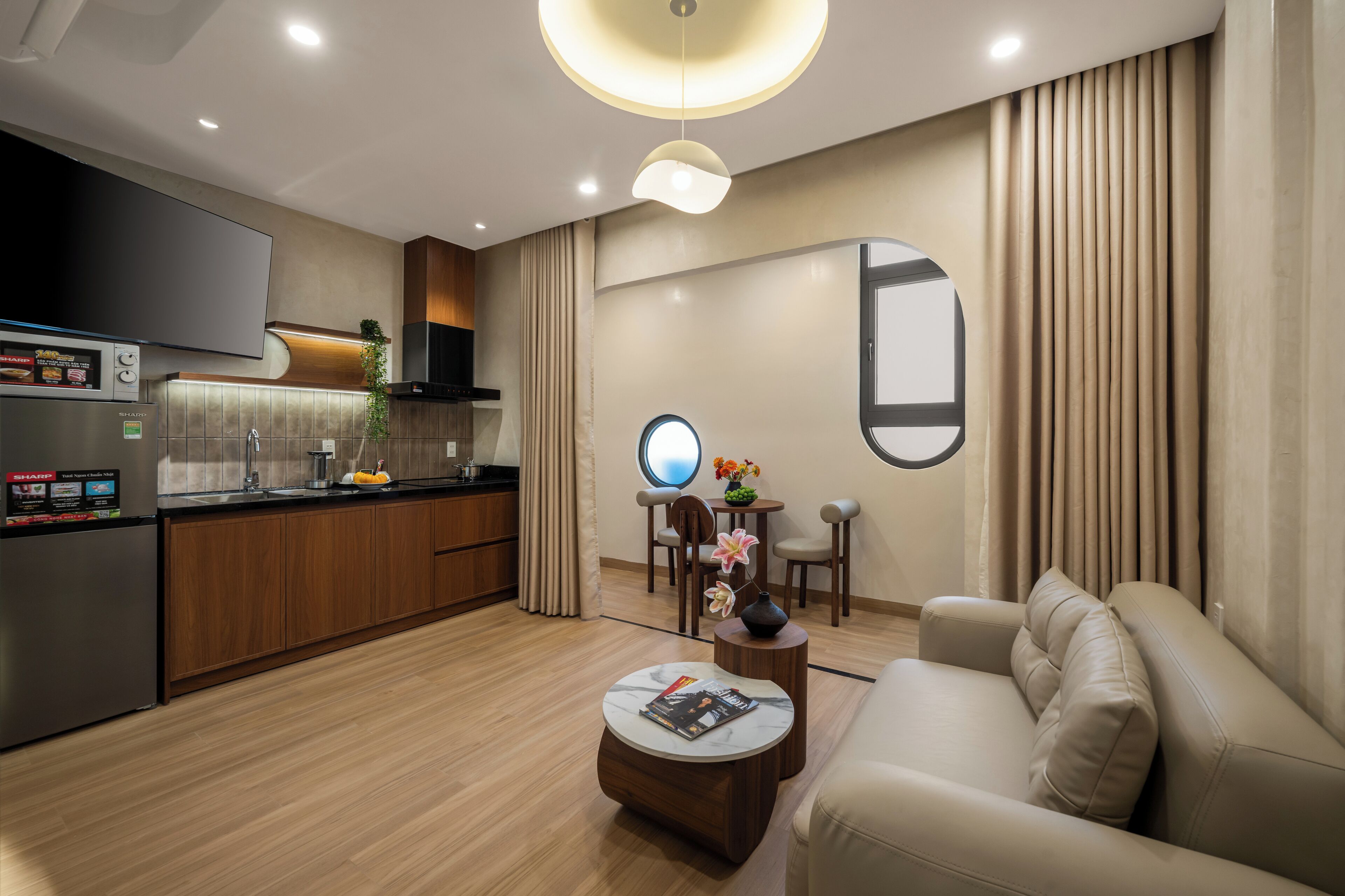 A modern living room with a sofa, a coffee table, a TV, and a kitchen area with wooden cabinets and a refrigerator.