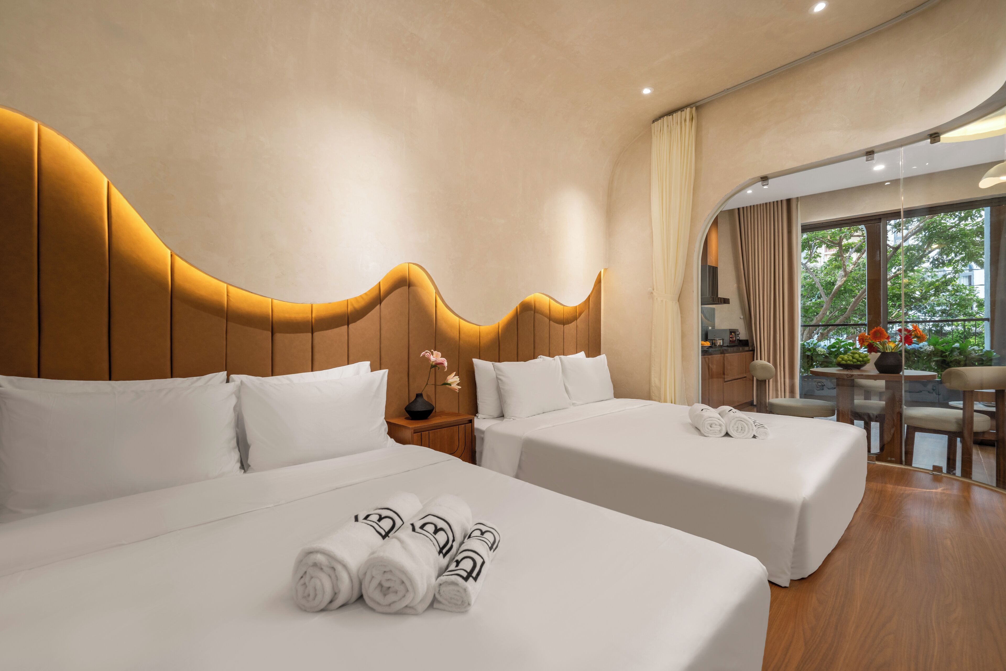 Een hotelkamer met twee bedden, een houten hoofdbord, een klein tafeltje met een bloevas en uitzicht op de omgeving.