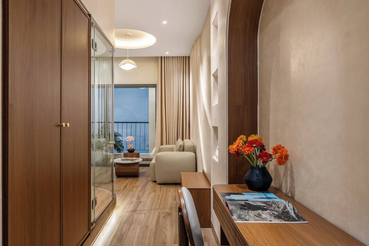 Ein modernes Hotelzimmer mit Holzboden, einem Essbereich mit Holztisch und -stühlen, einer Couch und Blick ins Freie.