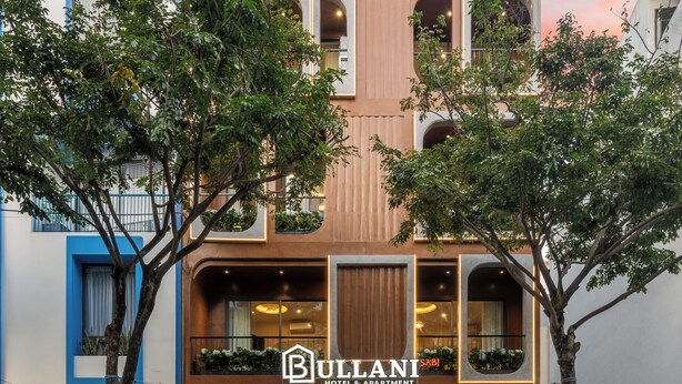 Un hôtel à la façade moderne, doté de balcons ornés de plantes et d’une enseigne indiquant « Bullani Hotel & Apartment ».