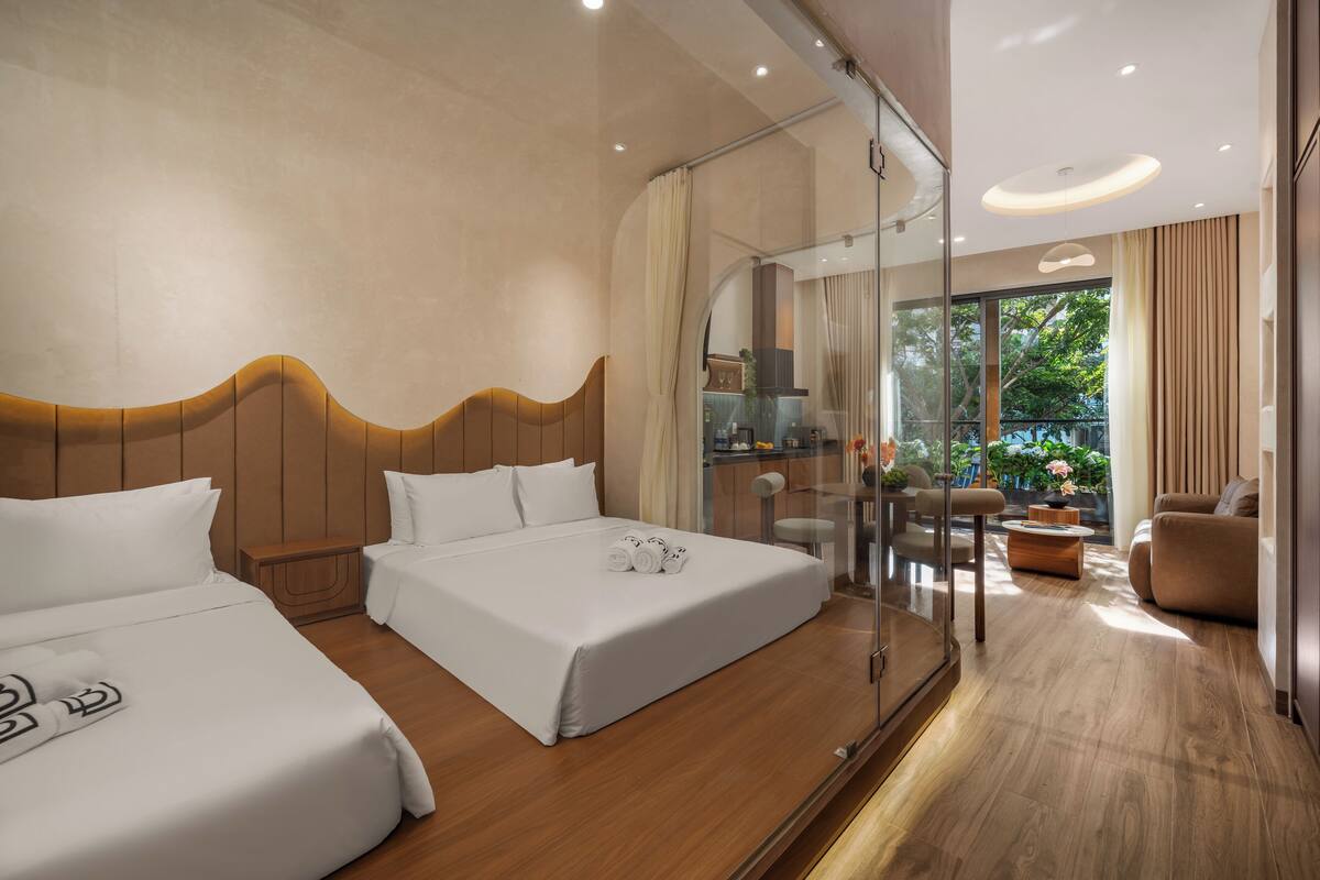 Ein modernes Hotelzimmer mit zwei Betten, einer Duschkabine aus Glas, einer Sitzecke mit Sofa und Sesseln sowie Blick ins Freie.