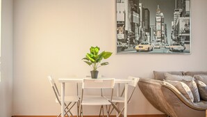 A dining area with a white table and chairs, a potted plant, and a cityscape painting on the wall. - Charming 2BR Apt in Prime Location (Vienna)