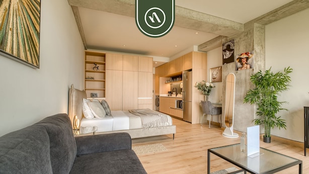 A modern living room with a grey sofa, a glass coffee table, and a kitchen in the background. - Stunning 1 BR Condo - Downtown - Alameda Central (Mexico City)
