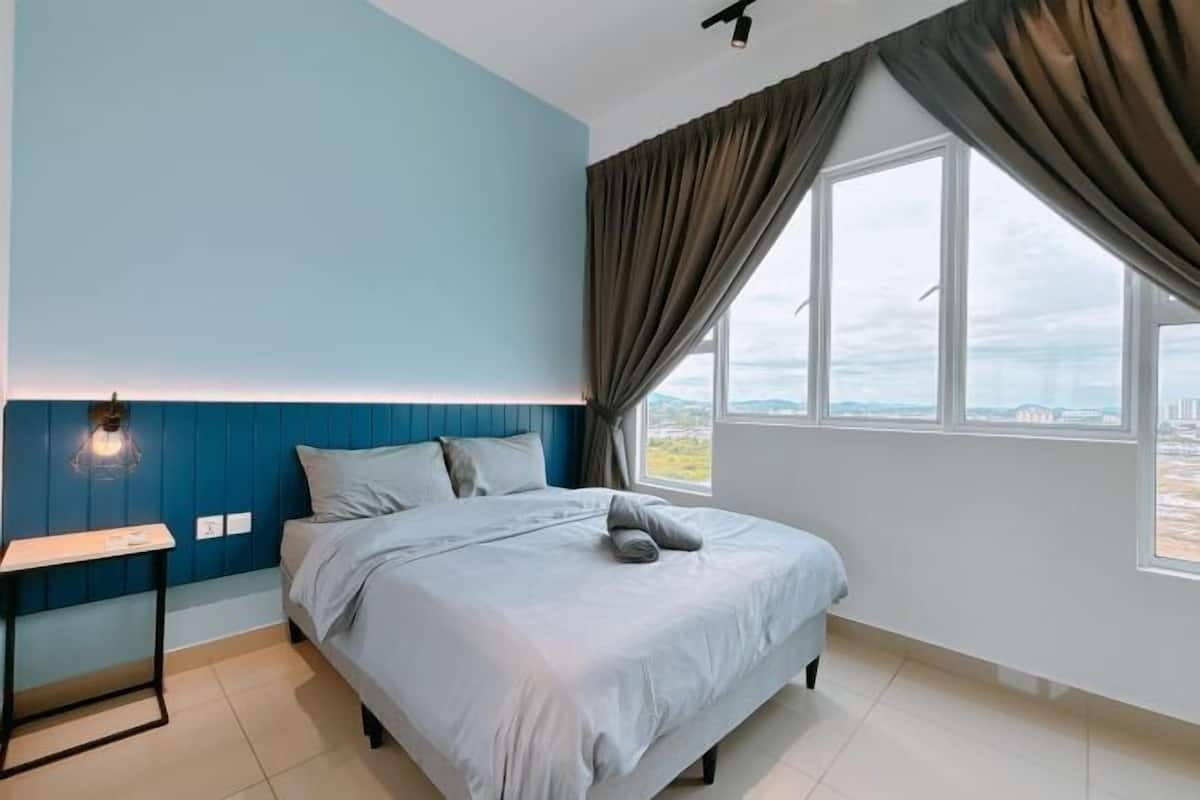 Quarto com cama, mesa de cabeceira, janela com cortinas e vista para o exterior.