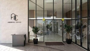 A modern hotel entrance with glass doors, a reception desk, and potted plants.