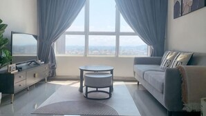 A modern living room with a sofa, a TV, a small table, and a view through a large window.