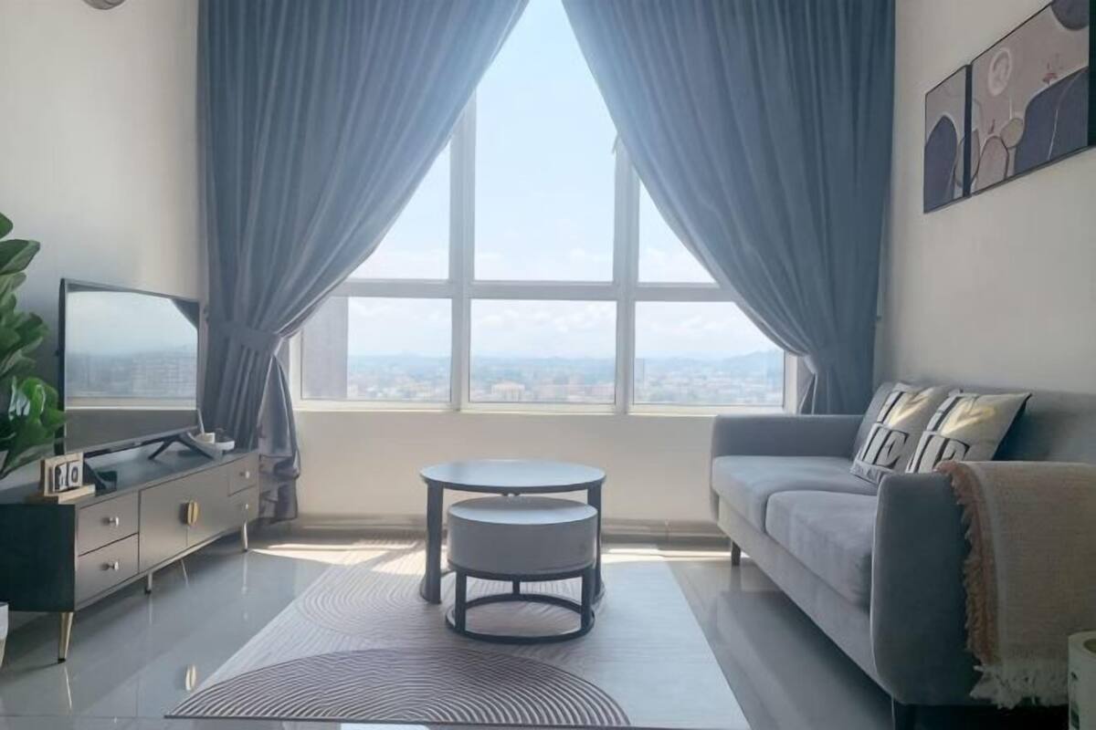 Uma sala de estar moderna com um sofá, uma televisão, uma mesinha e uma vista através de uma grande janela.