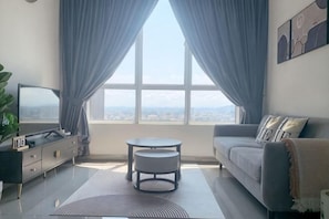 Ein modernes Wohnzimmer mit einer Couch, einem Fernseher, einem kleinen Tisch und Blick durch ein großes Fenster.