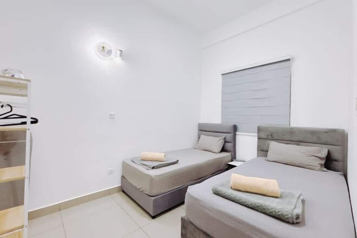 Quarto com duas camas, um guarda-roupa, uma luminária na parede e uma janela com persianas.