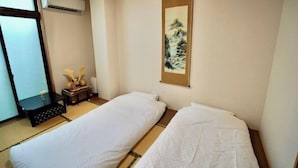 A room with two beds, a small table with a vase, a painting on the wall, and an air conditioning unit. - Nenenomichi (Kyoto)