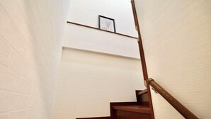 A narrow stairway with wooden steps and a wooden handrail, leading to a landing with a framed picture. - Nenenomichi (Kyoto)