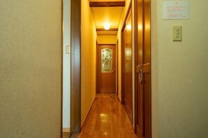 A narrow hallway with wooden flooring, a door at the end, and a light switch on the wall. - Tolai ryokan 1gokan (Atami)