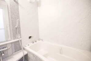 Een badkamer met een badkuip, douche, spiegel en een marmeren wand.