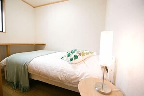 Een kleine, verzorgde slaapkamer met een enkel bed, een nachtkastje en een lamp.