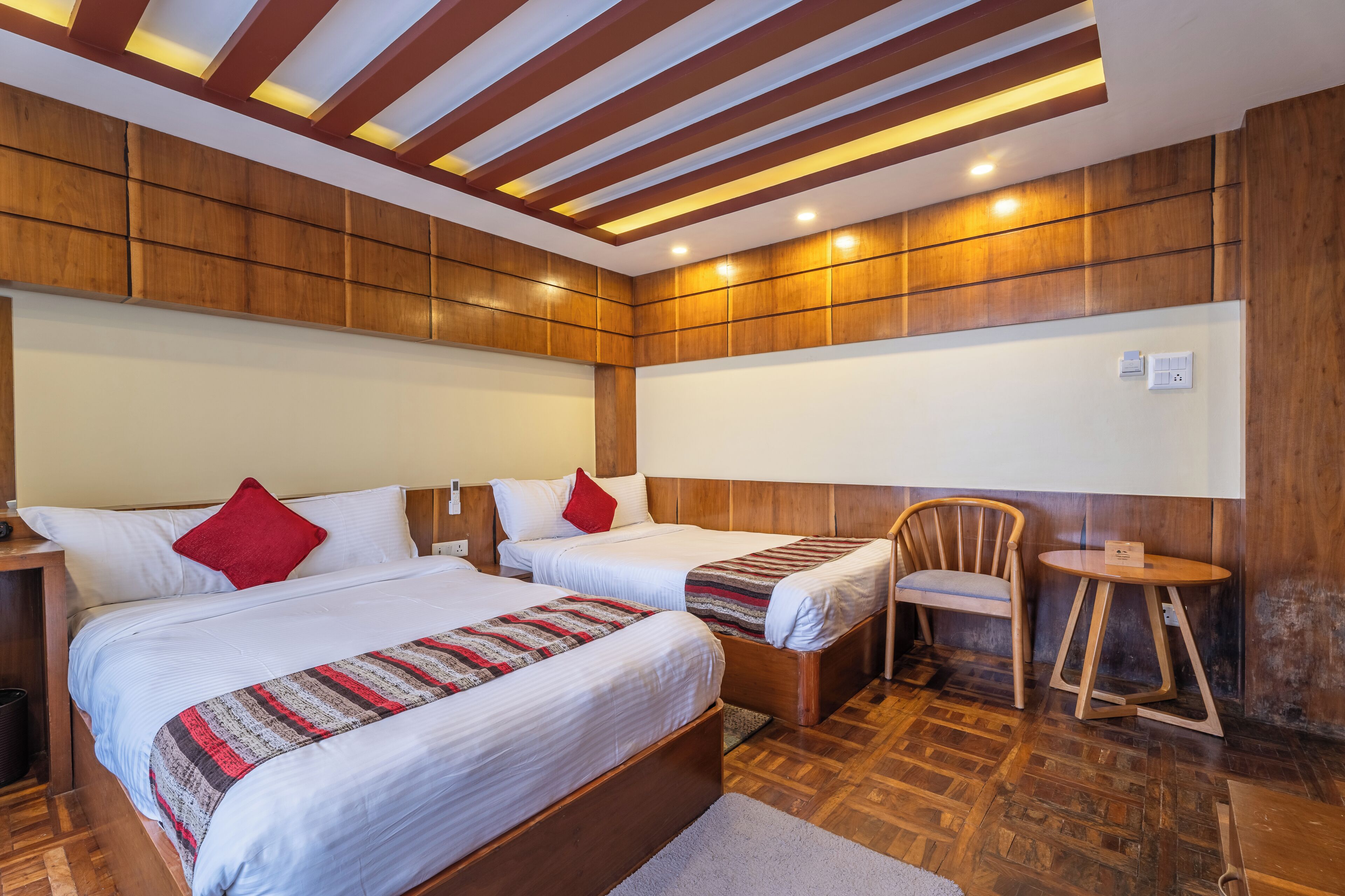 A hotel room with two beds, a wooden headboard, a small round table, and a chair.