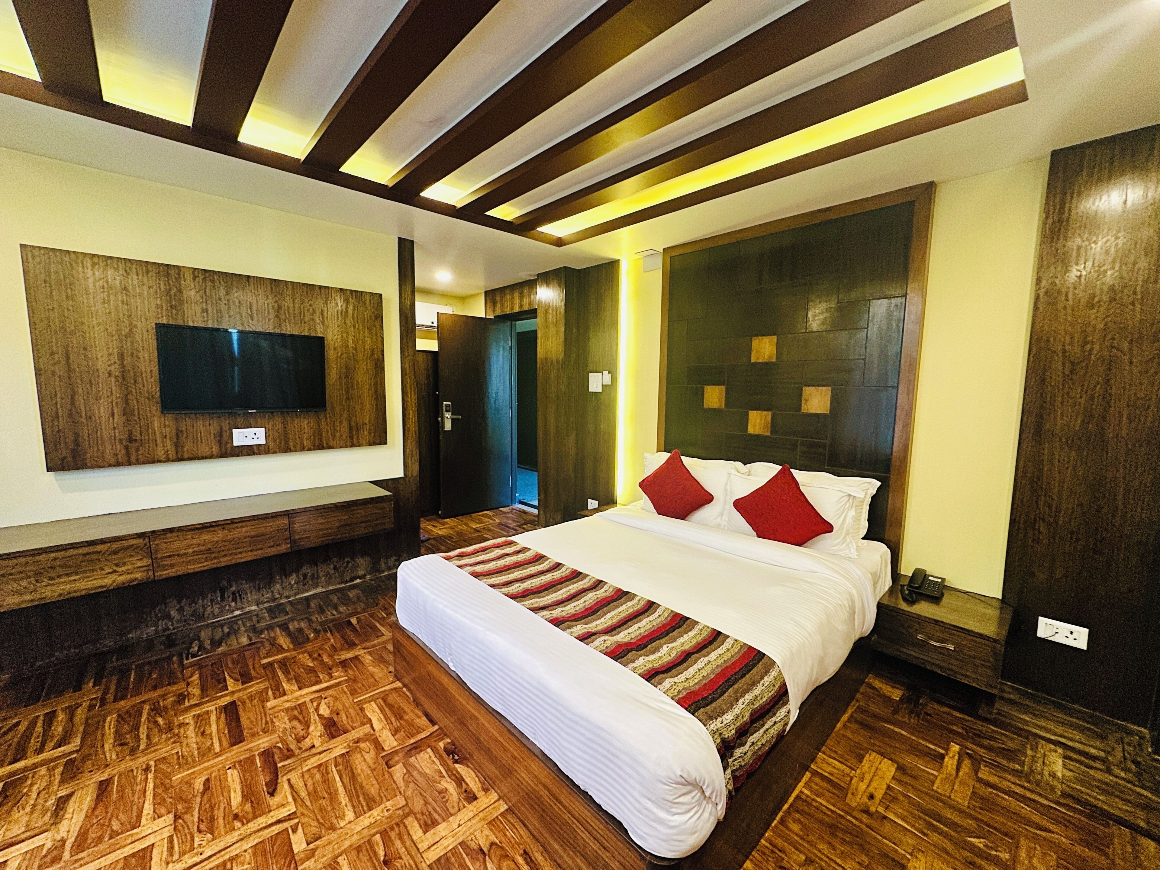 A hotel room with a large bed, wooden flooring, a mounted TV, and a modern headboard.