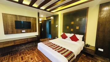 A hotel room with a large bed, wooden flooring, a mounted TV, and a modern headboard.