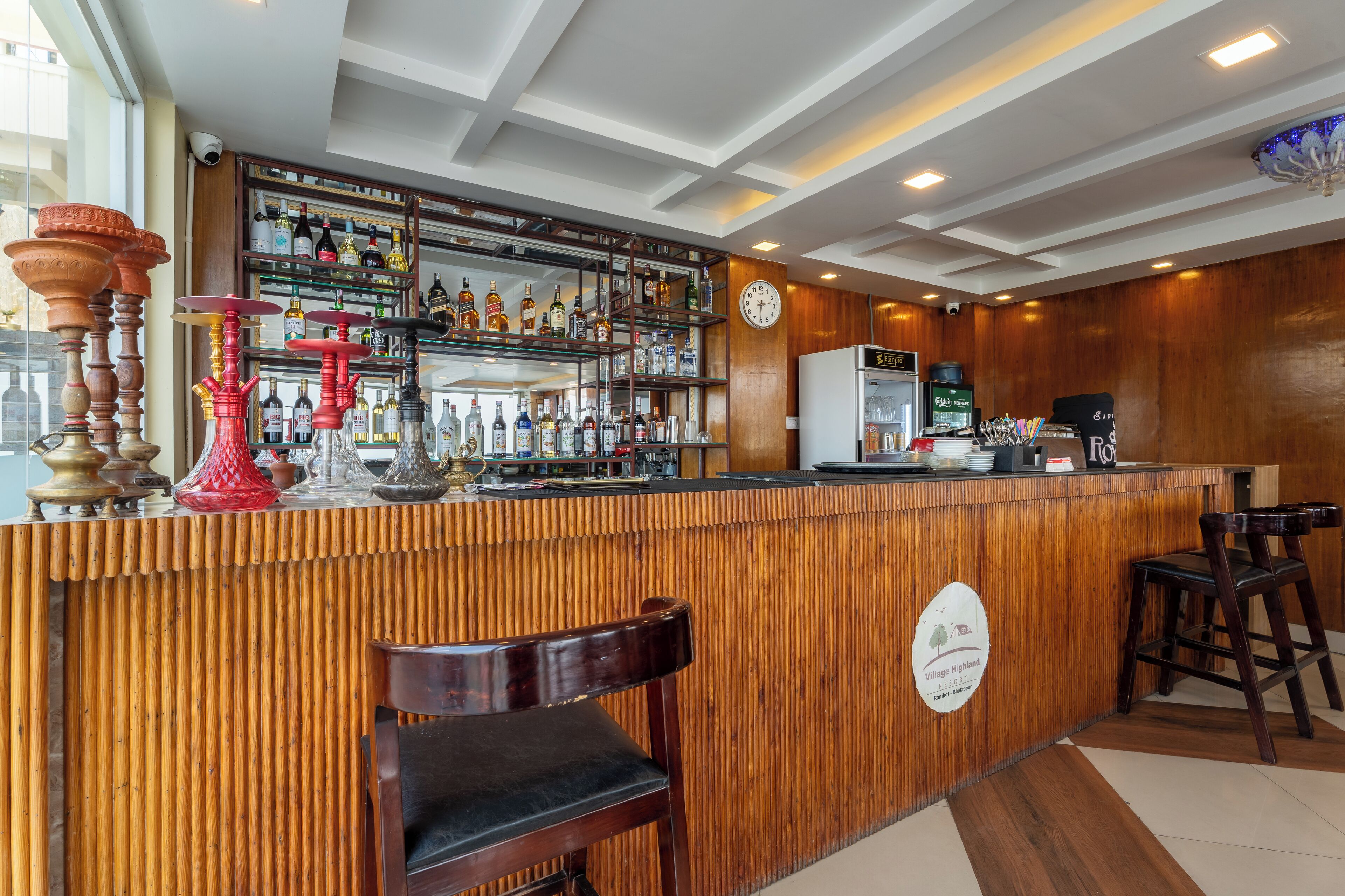 A bar area with a wooden counter, shelves of bottles, a clock, and a sign indicating a Village Highland Resort.
