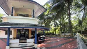 A modern building with a covered entrance, a car parked outside, and a paved area with palm trees in the background. - Dream House Near Iim Kozhikode & Nit Calicut (Kozhikode)