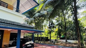A modern house with a car parked in the driveway, surrounded by lush greenery and palm trees. - Dream House Near Iim Kozhikode & Nit Calicut (Kozhikode)