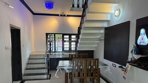 A modern interior with a staircase leading to a second floor, a dining area with a table and chairs, and a large flat-screen TV on the wall. - Dream House Near Iim Kozhikode & Nit Calicut (Kozhikode)