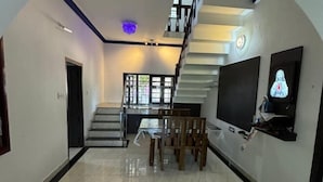 A spacious living area with a staircase, a dining table with chairs, and a television mounted on the wall. - Dream House Near Iim Kozhikode & Nit Calicut (Kozhikode)