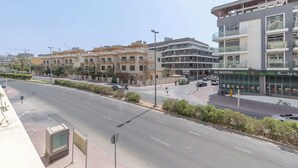 A modern urban street with multi-story buildings, a clear sky, and a few vehicles on the road. - JVC 1 bed for 3 People With Swimming Pool (Dubai)