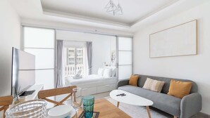 A modern living room with a grey sofa, a white coffee table, and a wooden dining table with clear glassware. - JVC 1 bed for 3 People With Swimming Pool (Dubai)