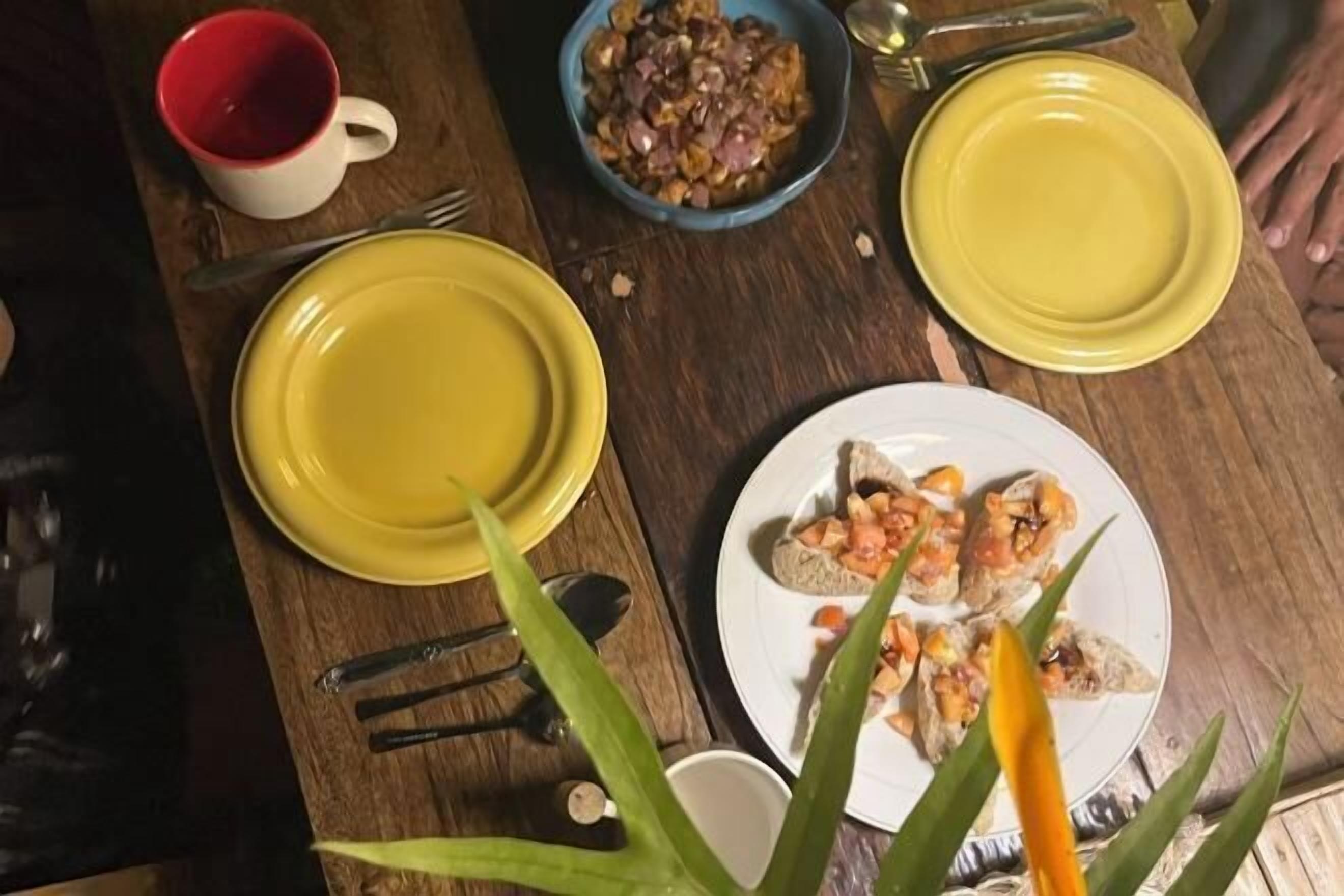 Una mesa de madera con platos amarillos, un bol de comida y una taza roja.