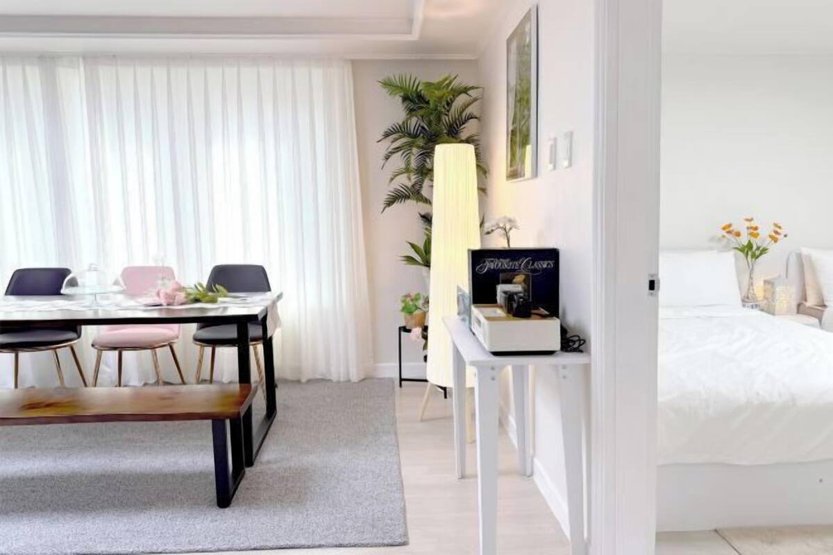 Ein Hotelzimmer mit einem Bett, einem Schreibtisch mit Lampe, einem Essbereich mit Stühlen und Tisch sowie einem großen Fenster mit Vorhängen.