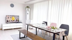 A modern living room with a dining table, bench, and a television on a white cabinet. - Hongik University Station 8min/Bedroom 3/Bed 4/Parking Available [Vanilla House] (Seoul)