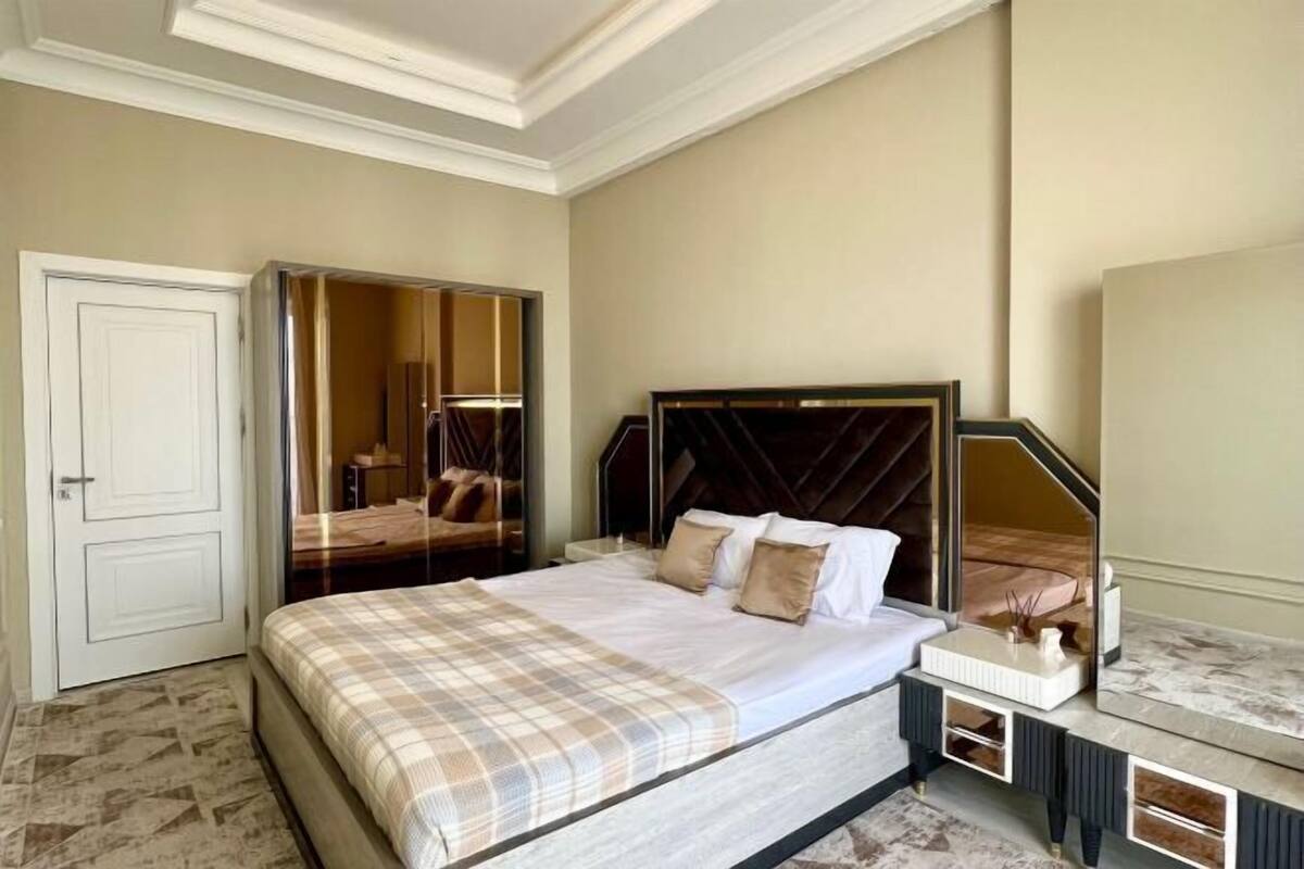 A bedroom with a bed, bedside table, mirror, wardrobe, and a door.
