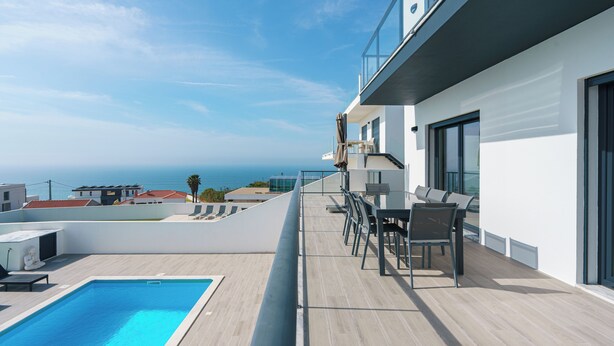 Une piscine sur le toit avec vue sur l’océan, un espace extérieur aménagé avec des sièges et une façade de bâtiment moderne.