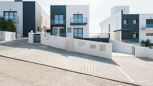 Un immeuble résidentiel moderne doté d’une allée pavée, d’une entrée sécurisée par un portail et d’un balcon au deuxième étage.