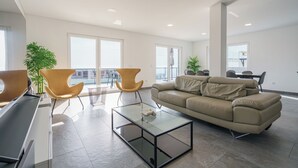 Un salon spacieux avec une table basse en verre, un canapé beige et deux fauteuils modernes.