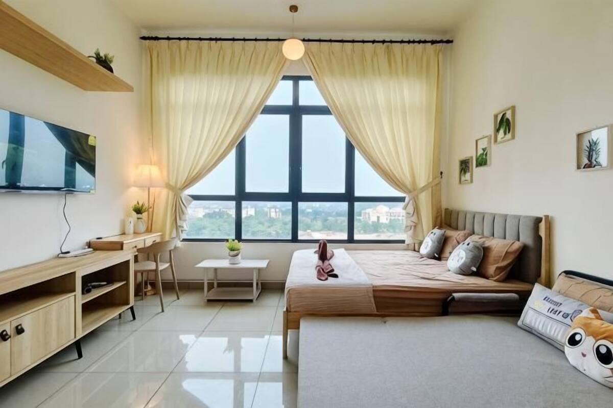 Quarto com cama, mesa de cabeceira, luminária, televisão e janela com cortinas.