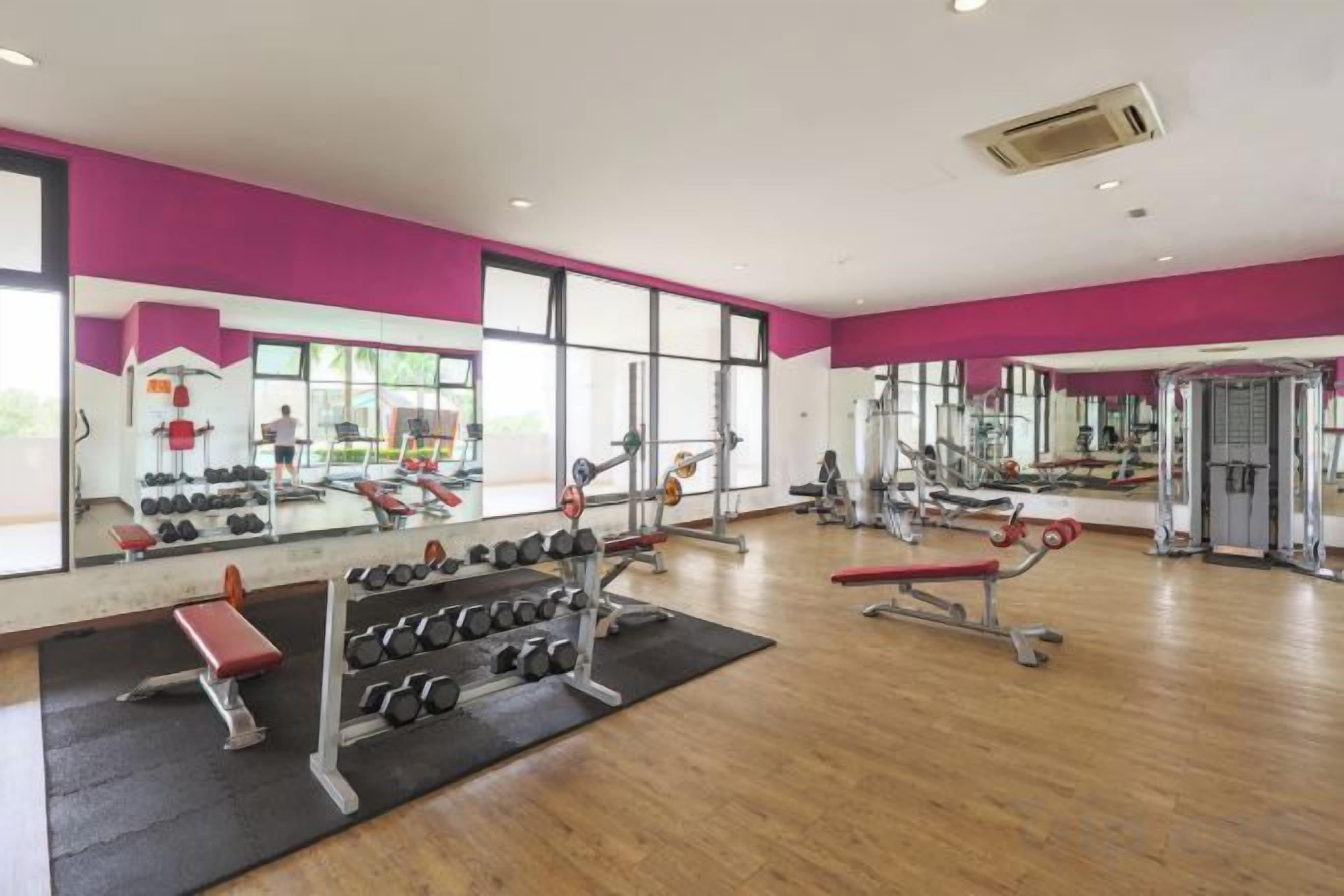 A gym with mirrored walls, various exercise equipment, and a large window providing natural light.