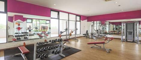 A gym with mirrored walls, various exercise equipment, and a large window providing natural light.