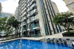 A high-rise building with a swimming pool, balconies, and surrounding greenery. - Lovely Unit with free wifi & netflix I across Naia Terminal 3 airport (Pasay)