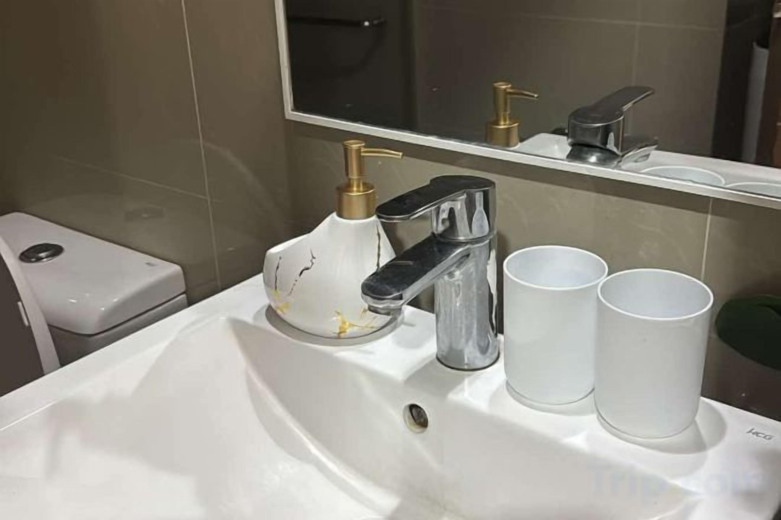 A bathroom with a white sink, a chrome faucet, a soap dispenser, and two white cups.
