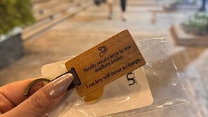 A hand holding a wooden key tag with a message about returning keys to the lobby. - Lovely Unit with free wifi & netflix I across Naia Terminal 3 airport (Pasay)