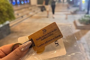 Una mano sostiene una etiqueta de madera con un mensaje sobre devolver las llaves a la recepción.