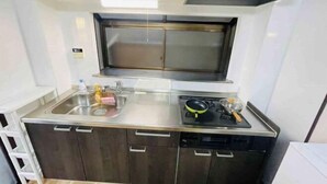 A compact kitchen with a stainless steel sink, a stove, and a window above the sink. - Remembrance (Osaka)