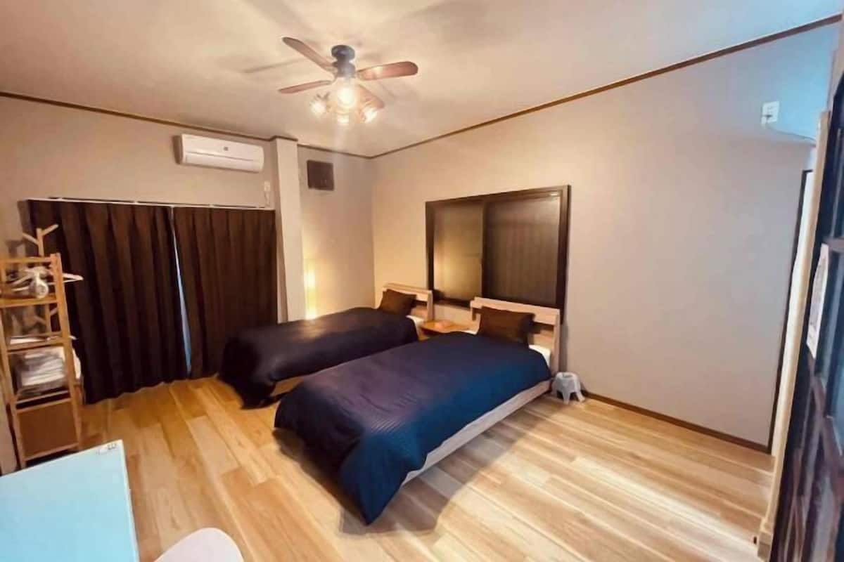 A hotel room with two beds, a ceiling fan, an air conditioning unit, and a wooden floor.